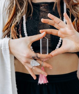A woman wearing jewelry holds a clear healing crystal, symbolizing spiritual wellness.